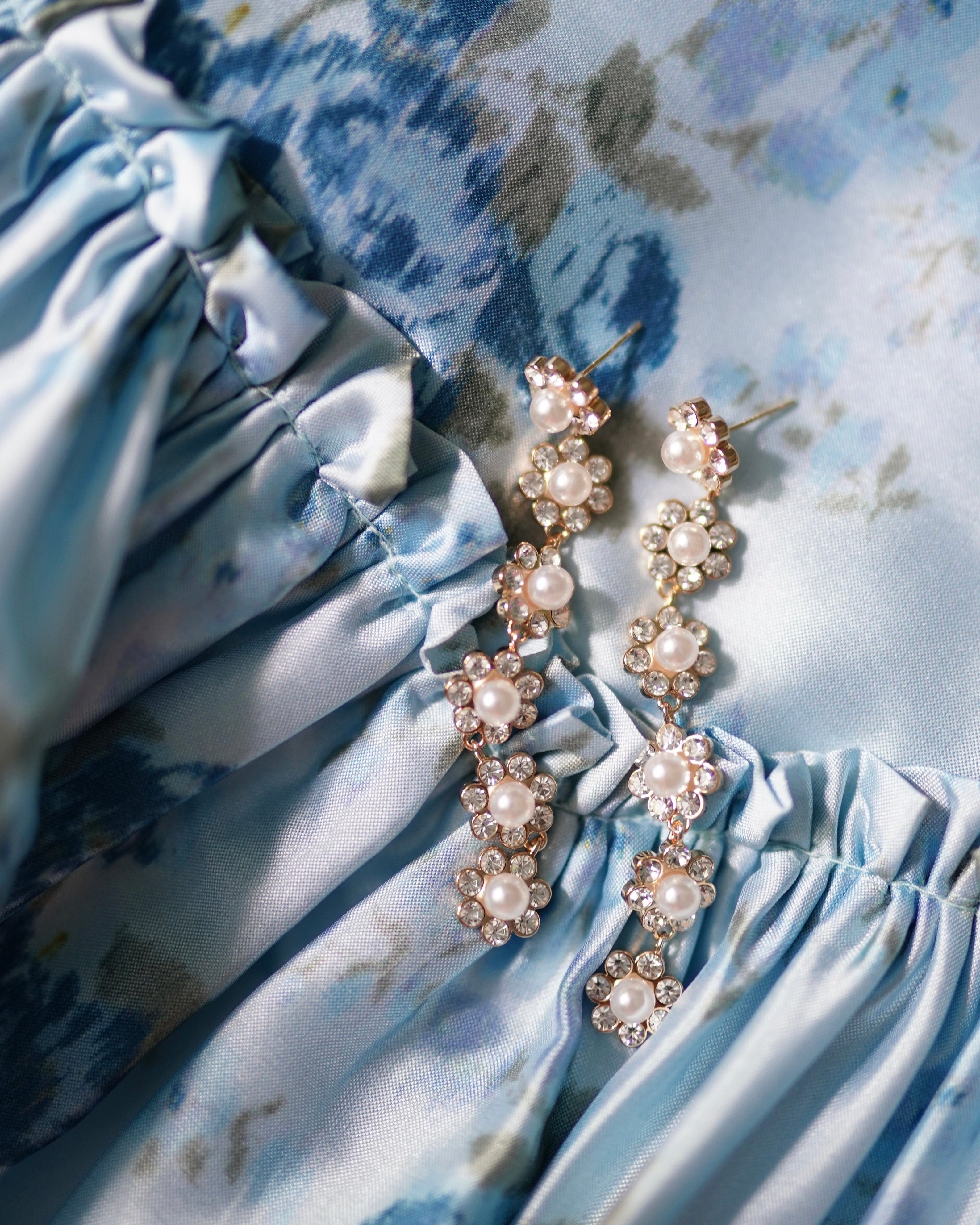 Crystal and pearl floral statement earrings on a blue and green floral fabric background