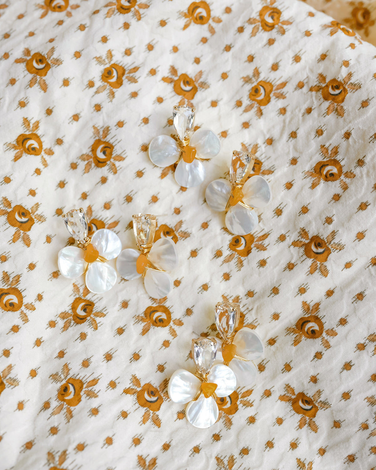 Orange and white mother of pearl earrings with crystals on an orange floral background 