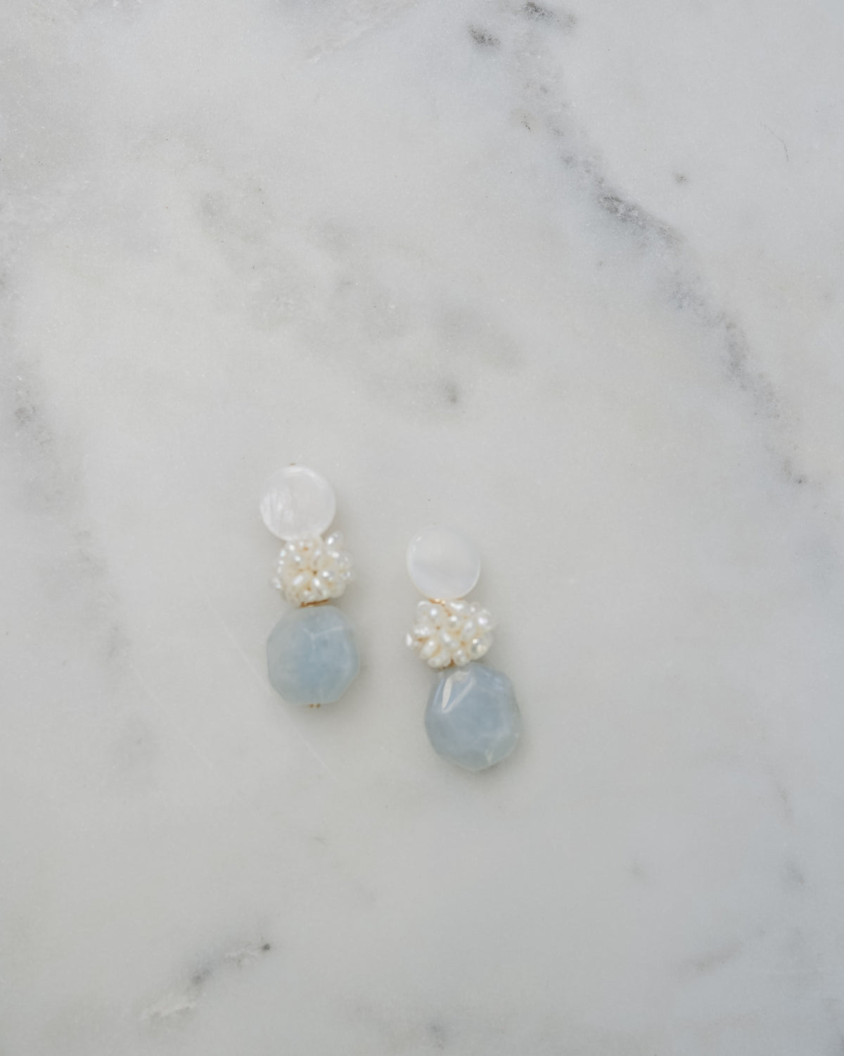 mother of pearl and aquamarine statement earrings on a white marble background