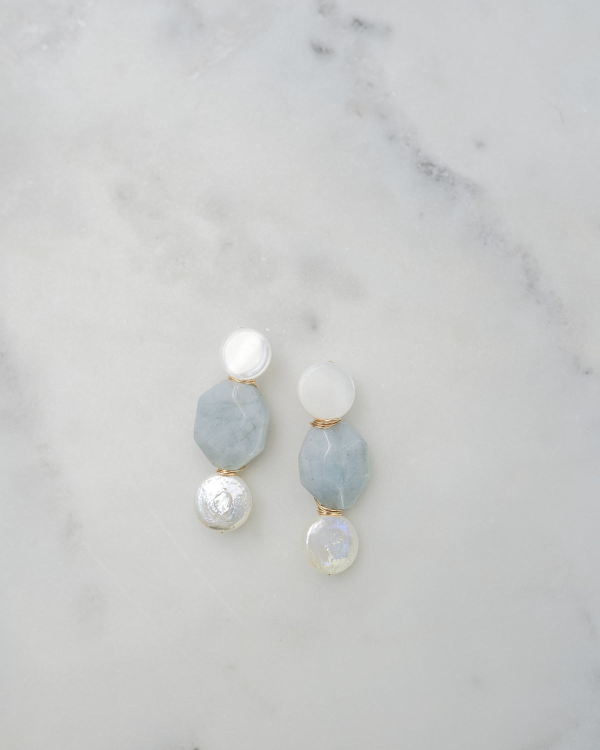 mother of pearl and aquamarine statement earrings on a white marble background