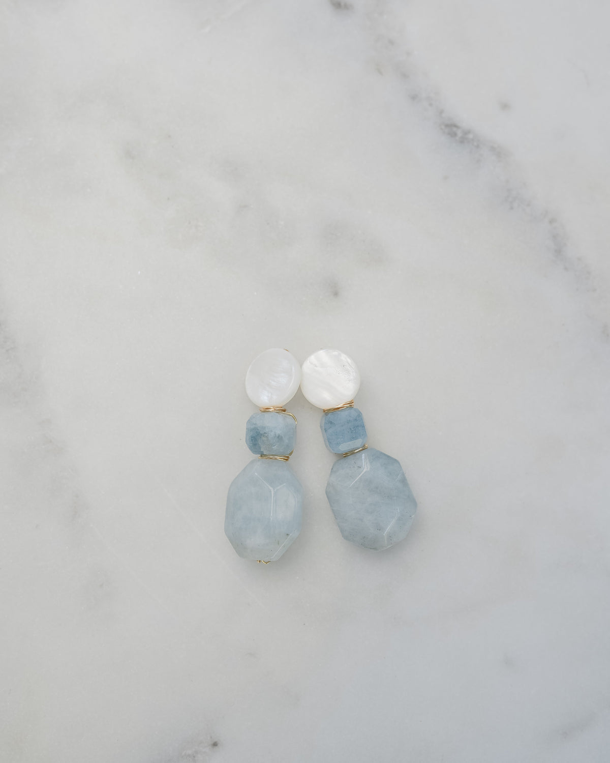 mother of pearl and aquamarine statement earrings on a white marble background
