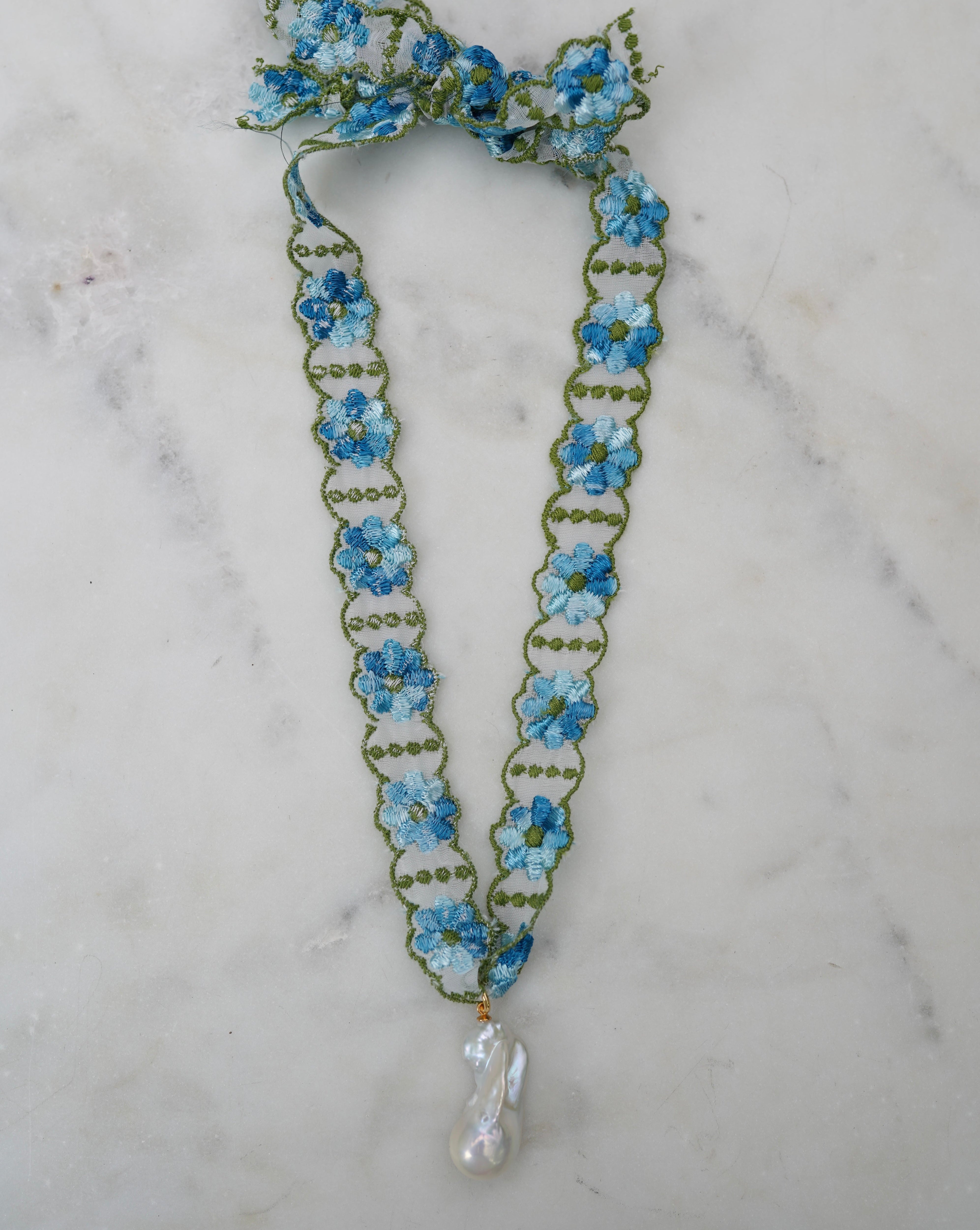 Floral necklace with blue flowers and a pearl drop on a marble background