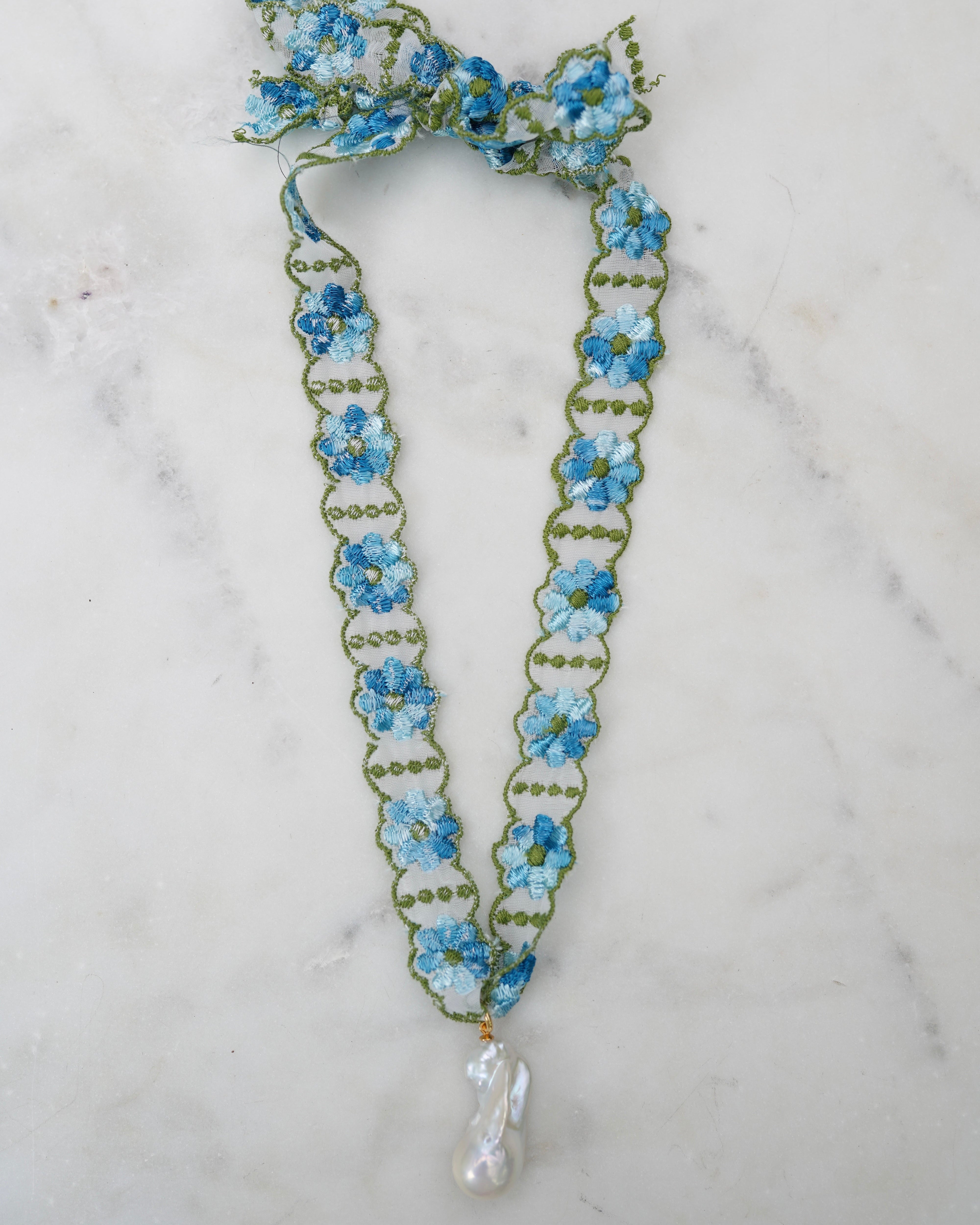 Floral necklace with blue flowers and a pearl drop on a marble background