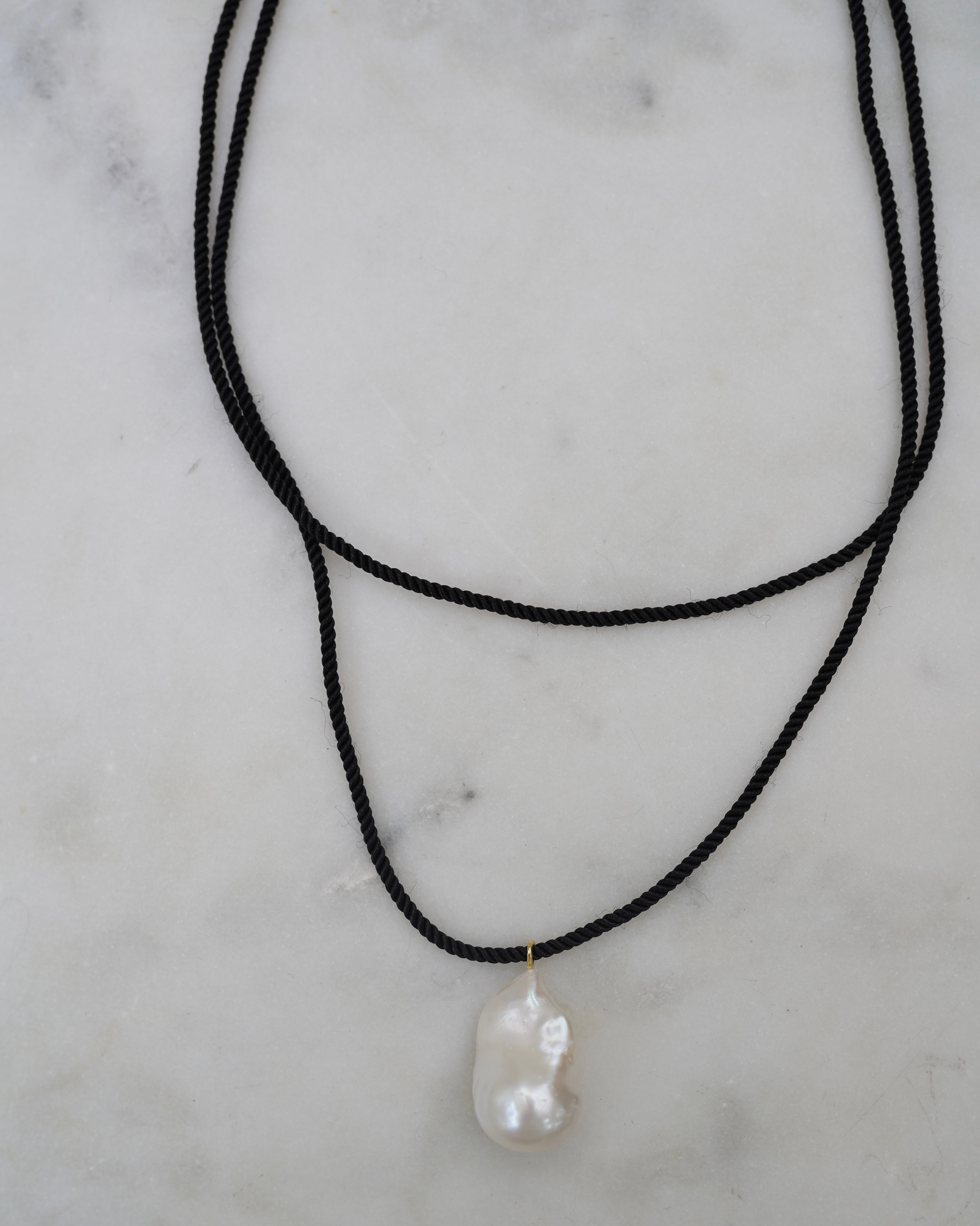Black cord necklace with a large pearl pendant on a marble surface