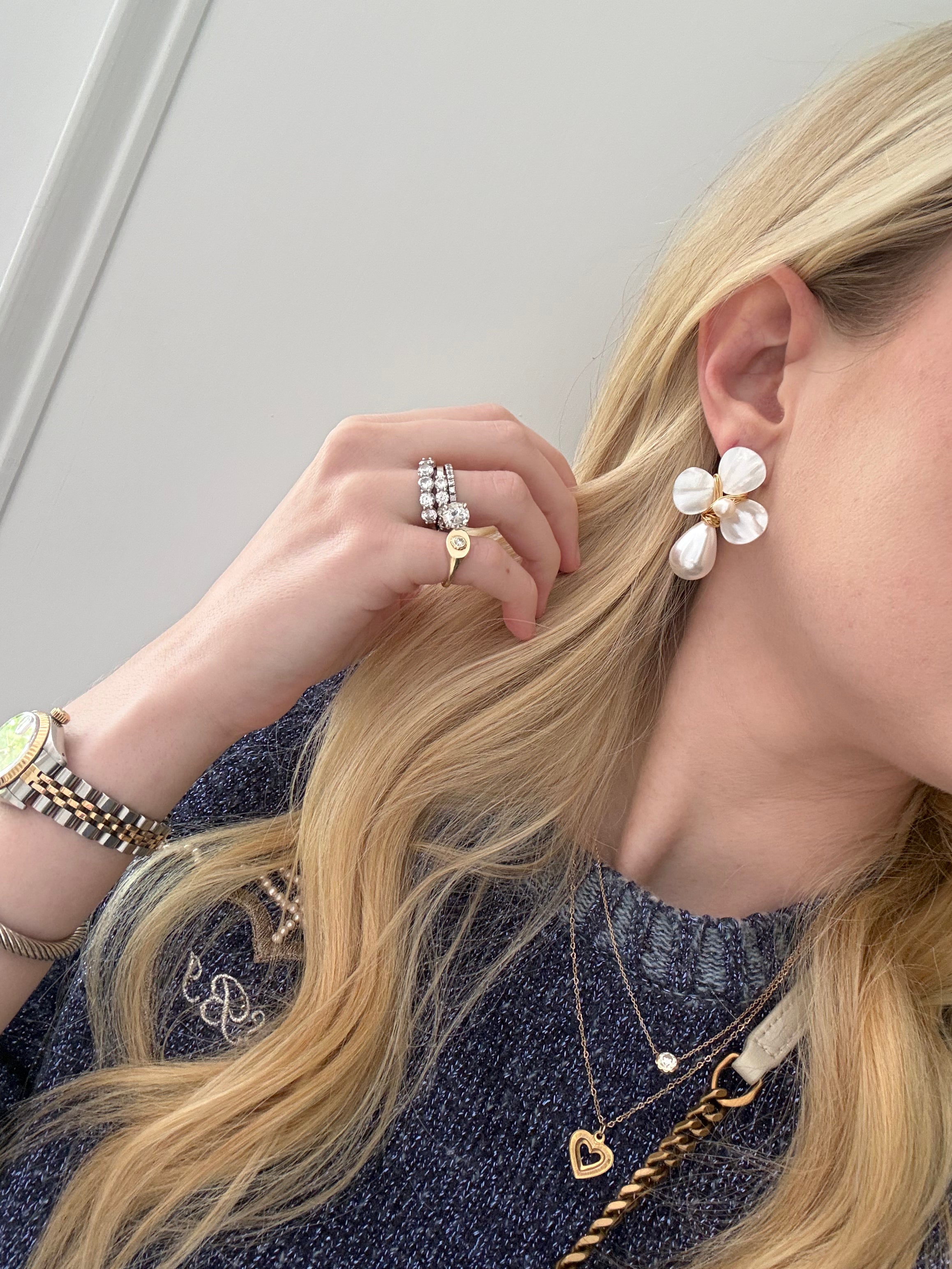 Woman wearing a floral earring and multiple necklaces with a plain background