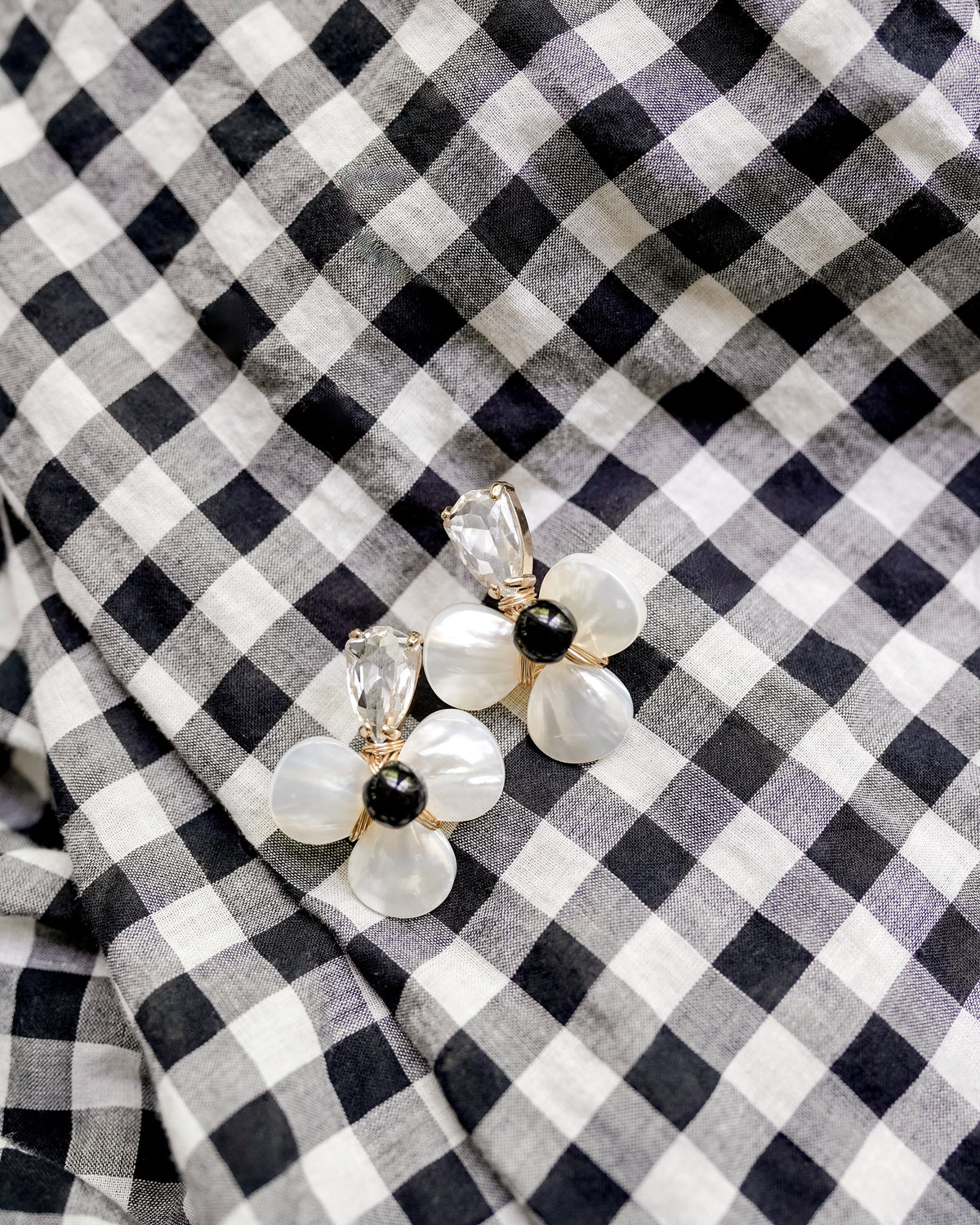 Crystal and mother of pearl flower shaped earrings with a black stone center on a black and white gingham background