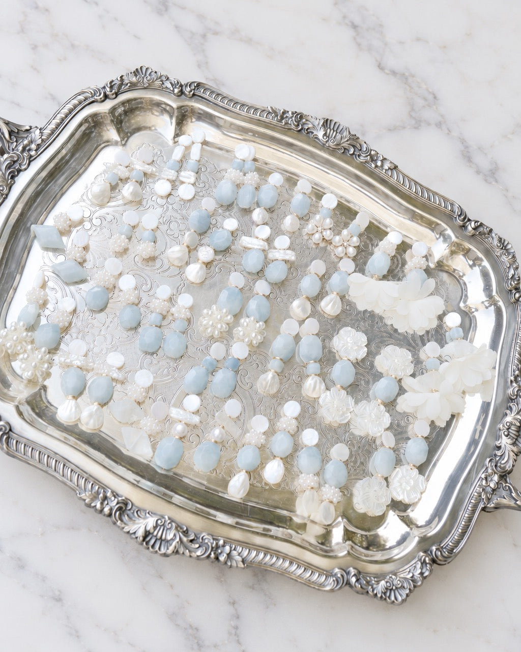 mother of pearl and aquamarine statement earrings on a silver tray on a white marble background